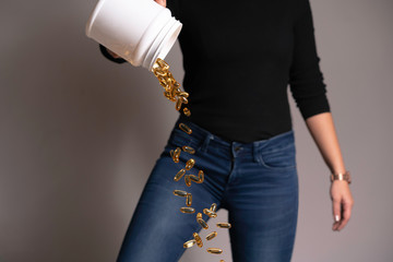 Young woman playing, throwing or wasting many omega 3 or fish oil yellow pills from the jar