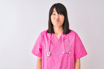 Young beautiful Chinese nurse woman wearing stethoscope over isolated white background puffing cheeks with funny face. Mouth inflated with air, crazy expression.