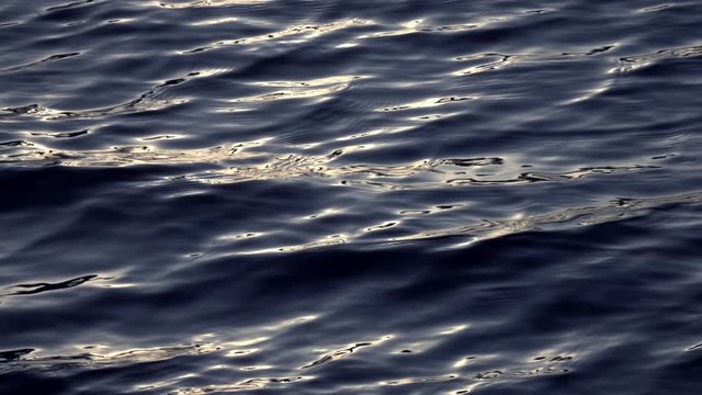 Slow motion of fluent ripple on dark water surface with reflection of low sun close up. Amazing meditative background for excellent intro in hypnotic style. Liquid metal mirror with natural pattern.