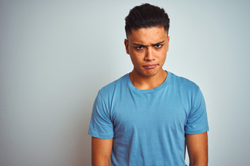 Obraz premium Young brazilian man wearing blue t-shirt standing over isolated white background skeptic and nervous, frowning upset because of problem. Negative person.