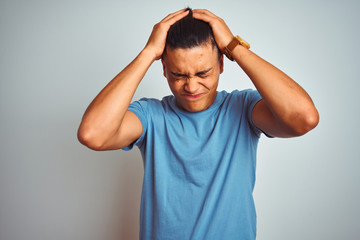 Fototapeta na wymiar Young brazilian man wearing blue t-shirt standing over isolated white background suffering from headache desperate and stressed because pain and migraine. Hands on head.