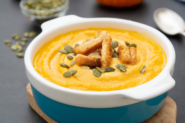 Pumpkin soup in a bowl,with fresh pumpkin seeds. Autumn foods. Healthy, vegetarian food, dark background.