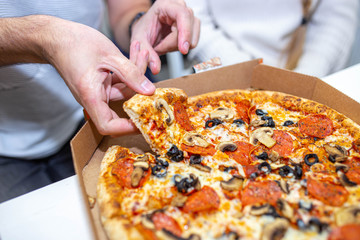 eating vegetarian pizza with tomatoes and olives. hands hold a slice of pizza.