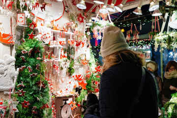 Naklejka premium Woman buying Ceramics Christmas Tree Decorations on Night Market in Gendarmenmarkt in Winter Berlin, Germany. Advent Fair and Bazaar Stalls with Craft Items.