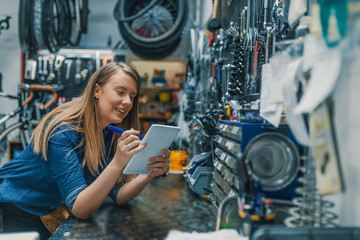Side view of smiling young woman using digital tablet while working in bike service.