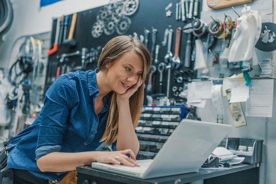 Portrait of beautiful working woman in the bicycle store. Young female mechanic with laptop. Female Bicycle Mechanic. Craftswoman working using a laptop in the garage