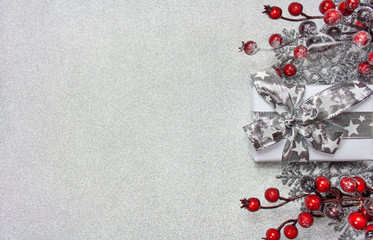 Bożonarodzeniowe srebrne tło z prezentem, gałązkami pokrytymi czerwonymi jagodami oraz srebrnymi gwiazdkami - obrazy, fototapety, plakaty