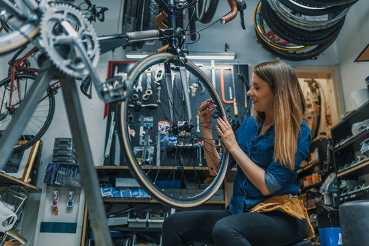 Bike service: mechanic servicewoman repairman installing assembling or adjusting bicycle gear on wheel in workshop. Young woman working in a biking repair shop