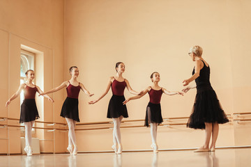 Graceful ballerinas practicing with mature instructor at ballet studio.