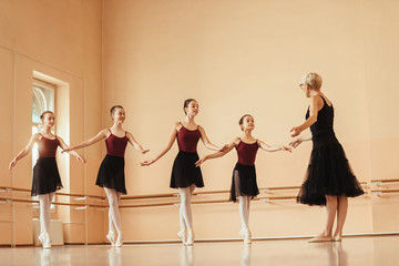 Naklejka premium Graceful ballerinas practicing with mature instructor at ballet studio.
