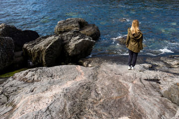 A girl walks on the stones of coastline near the ocean. Beautiful nature landscape in North. Scenic outdoor view. Enjoy the moment, relaxation. Wanderlust. Travel, adventure, lifestyle. Explore Norway