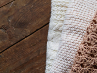 White, beige and brown knitted sweaters on shabby wooden background.