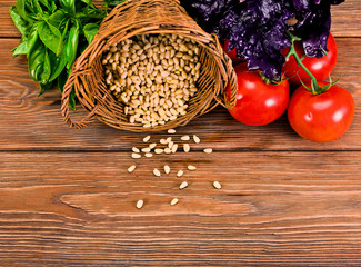 Fresh ingredients for preparing pesto sauce - basil leaves, peeled seeds of cedar nuts and tomatoes on a wooden background. Top view.