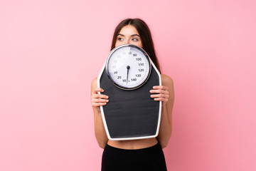Pretty young girl with weighing machine over isolated pink background with weighing machine and...