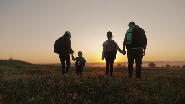 Parents and two children walking in the mountains at the sunset time. Silhouette happy beautiful family during the travelling. Concept of friendly family and travel.