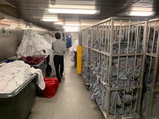 Cleaner is walking in yhr huge laundry on a cruise ship. A lot of white dirty linen and grey pool...