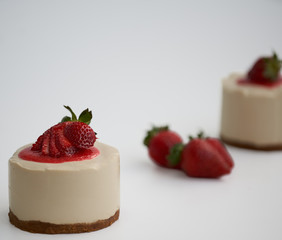 Cheesecake with strawberry sauce and fresh strawberries and another cake out of focus in the background 