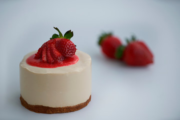 Close-up of a homemade cheesecake with strawberry sauce and fresh strawberries out of focus in the background 