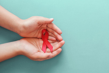 Hands holding red ribbon on blue background, hiv awareness concept, world AIDS day, world hypertension day - obrazy, fototapety, plakaty
