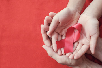 Hands holding red ribbon on red background, hiv awareness concept, world AIDS day, world...