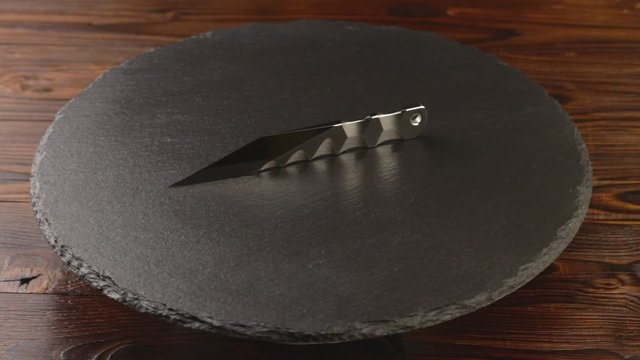 Custom hand crafted japanese kiridashi knife on the turning slate board table. Polished metal surface with texture