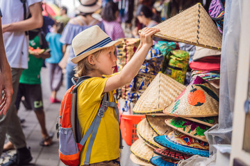 Fototapeta na wymiar Boy at a market in Ubud, Bali. Typical souvenir shop selling souvenirs and handicrafts of Bali at the famous Ubud Market, Indonesia. Balinese market. Souvenirs of wood and crafts of local residents