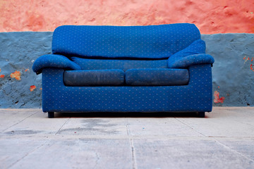 Abandoned blue couch in a colorful backyard, alternative economy outdoor furniture concept.