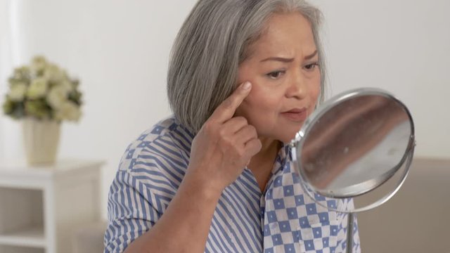 Old woman is looking in the mirror the face wrinkle