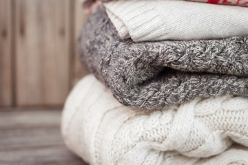 Stack of cozy knitted sweaters on wooden background. Autumn, winter concept