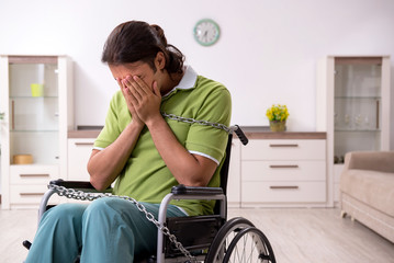 Young male invalid in wheel-chair suffering at home