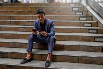 Young business man using credit card for online payment via mobile phone, sitting at stairs at city
