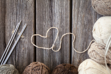 White knitting wool and knitting needles with heart. Wooden background, natural wool knitting background