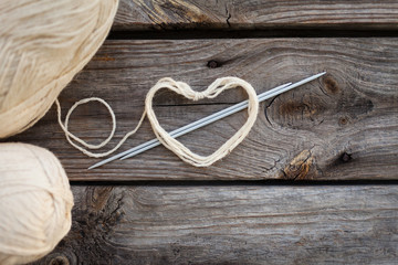 White knitting wool and knitting needles with heart. Wooden background, natural wool knitting...
