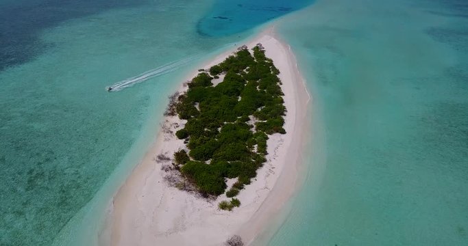 Paradise tropical island surrounded by clear calm emerald water of lagoon with coral reefs and pebbles, young man tracing with ski jet in Maldives