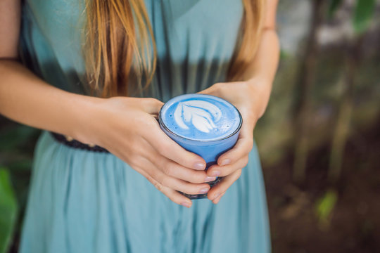 Young woman having a mediterranean breakfast seated at sofa and drinks Trendy drink: Blue latte. Hot butterfly pea latte or blue spirulina latte