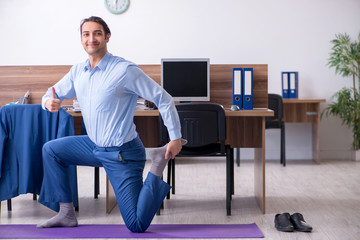 Young handsome businessman doing exercises at workplace