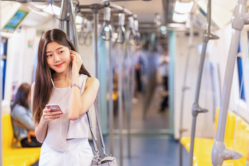 Young Asian woman passenger listening music via smart mobile phone in subway train when traveling...