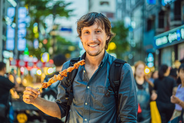 Young man tourist eating Typical Korean street food on a walking street of Seoul. Spicy fast food...