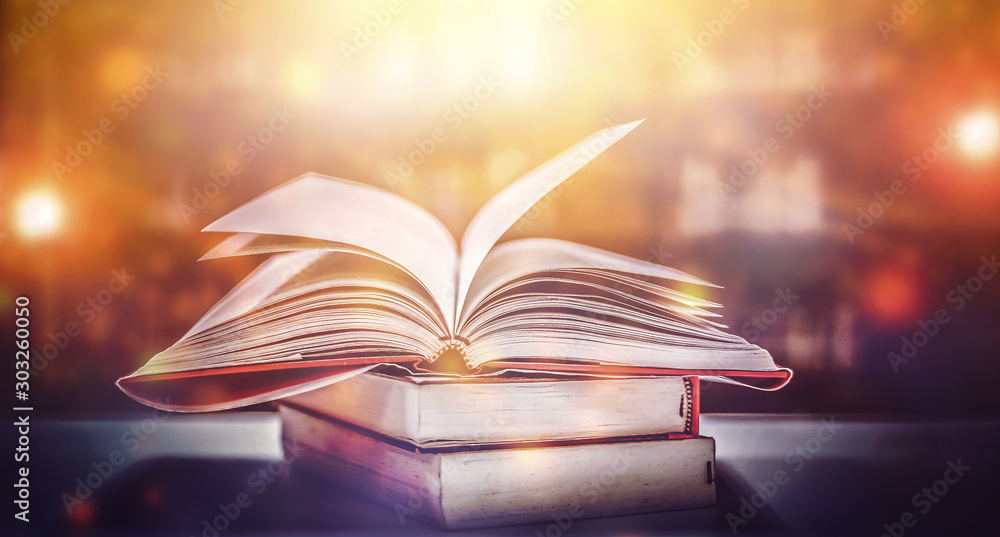 Poster book in library with old open textbook, stack piles of literature text archive on reading desk, and 