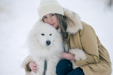 A young girl walks in winter with a white Samoyed dog in a snowy meadow in the forest.