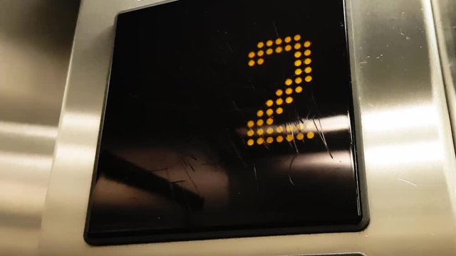 Closeup of numbers in elevator from 1 to 4 moving going on dark screen with lights.