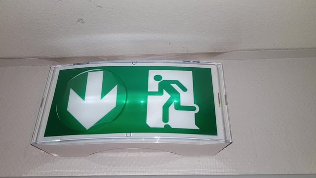 The exit sign on the wall of the corridor on the green eran inside of house
