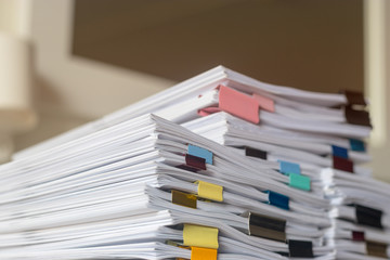 Pile of student homework that assigned to student to be completed outside class on teacher desk separated by colored paper clips. Document stack arranged by paperclip. Business and education concept.