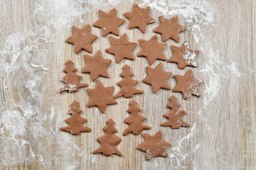 Unrolled spiced dough sliced ​​in cookie cutters on baking paper on a wooden table. Christmas, winter, new year. Fir-trees, stars, flour.