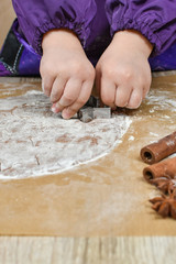 Children's hands cut out cookie dough with cookie cutters.