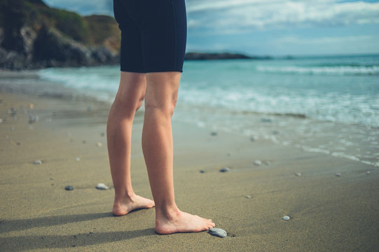The legs and feet of a young woman in wetsuit on the beach