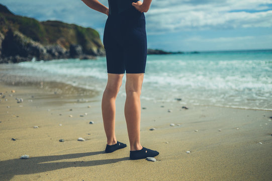 The legs and feet of a young woman in wetsuit on the beach