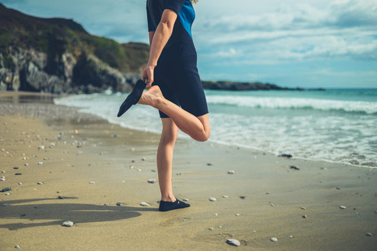 Woman in wetsuit on the beach putting on waterproof shoes