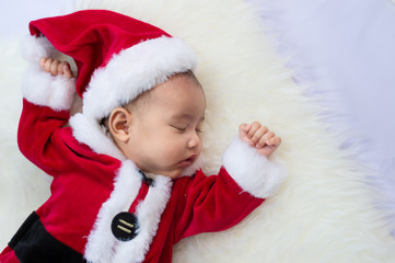Fototapeta premium baby girl wearing red Santa Claus costume sleep on white fur carpet. Concept of celebrates Christmas and New Year's holidays.