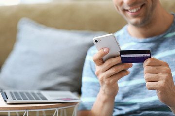 Young man with credit card and mobile phone at home, closeup